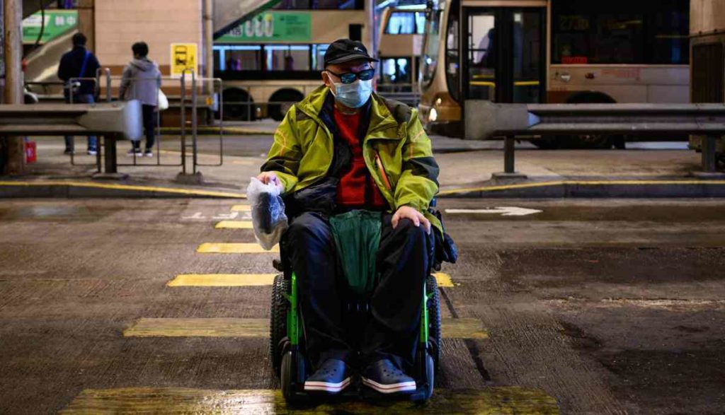 Persona con discapacidad trasladándose con protección frente al covid-19 con su silla de ruedas.